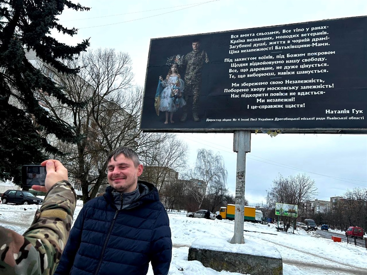Захисник фотографується біля бігборду, на якому є вірш Наталії Гук